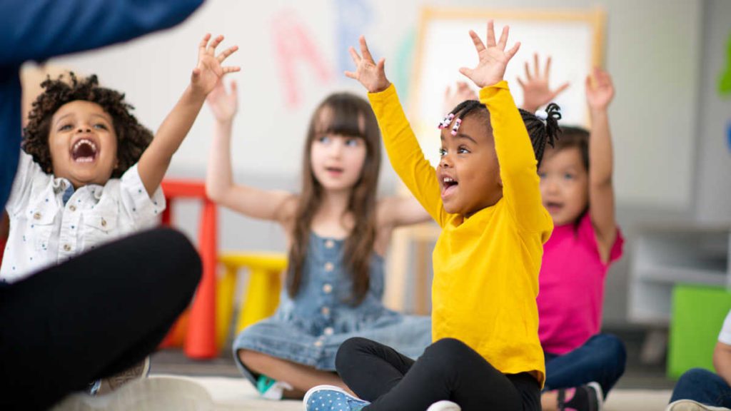 Young children sing in a classroom setting with a teacher.