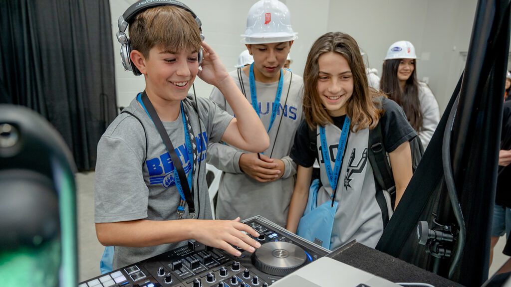 A pre-teen boy operates a digital DJ deck as fellow 7th-grade students look on as part of the HEA Career Quest event.