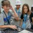 A pre-teen boy operates a digital DJ deck as fellow 7th-grade students look on as part of the HEA Career Quest event.