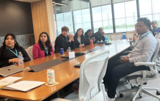 Youth apprentices and employers sit around a conference room table listening to a presentation.